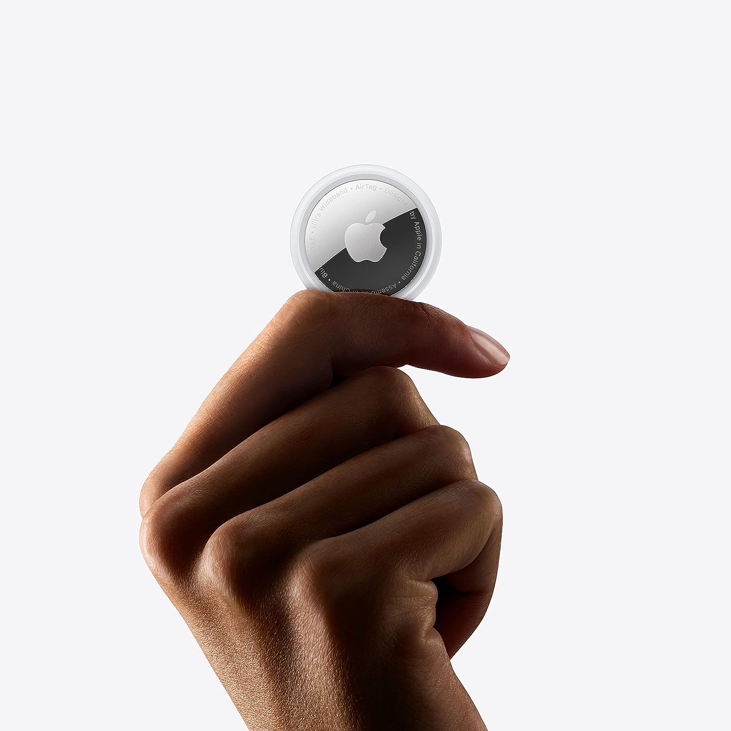 The image shows a person's hand holding a small, circular device with an Apple logo on it. This device is known as an AirTag, designed by Apple. The AirTag is a small tracking device that can be attached to personal items such as keys, wallets, or bags to help locate them using Apple's Find My network. The background of the photo is a plain, light color, providing a clear and high-contrast backdrop for the item and hand.