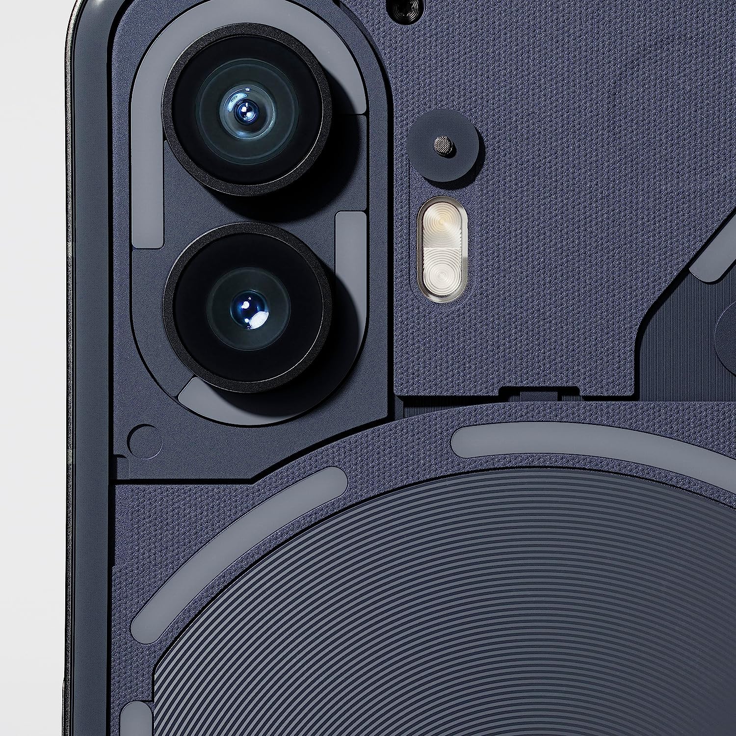 This image appears to be a close-up view of the camera system of the nothing phone 2. The visible features include two camera lenses, which could indicate a dual-camera setup often used for improving photo capabilities such as zoom and depth perception. There's also a flash module next to the camera lenses, and what seems to be a microphone hole for noise cancellation or audio recording. The textured material around the camera module could be part of the phone's back cover design, which is often crafted for aesthetic appeal as well as grip enhancement. The design and complexity of the camera system indicate it is likely a high-end or flagship model of a smartphone.