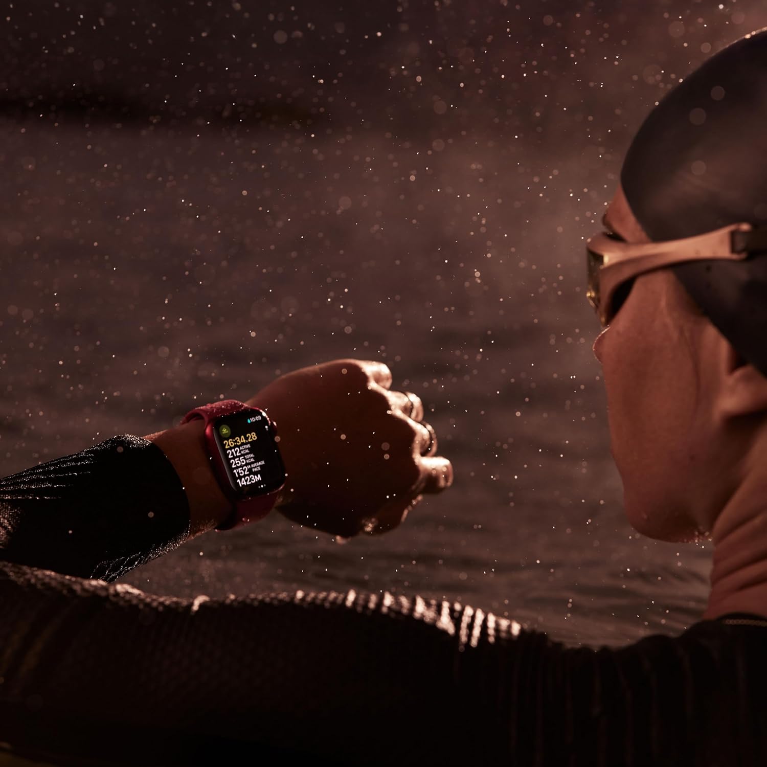 The image features a close-up of a swimmer's arm coming out of the water, with water droplets captured in mid-air. The swimmer is wearing an Apple Watch Series 9 on their wrist, which seems to display data such as duration, heart rate, and other metrics that might be related to a swimming activity. Additionally, the swimmer is wearing swim goggles and a swim cap, indicating that they are engaged in a swimming exercise or competition. The lighting and focus on the water droplets create a dynamic and intense atmosphere.