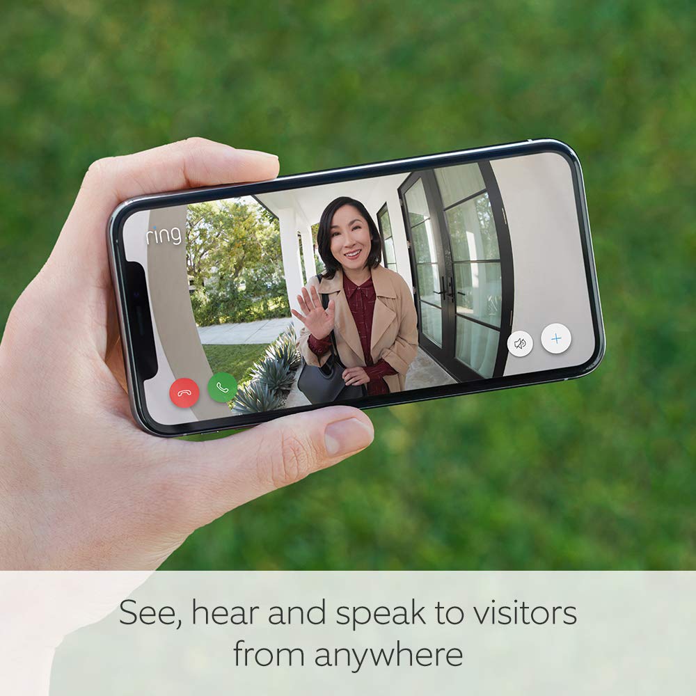 This image displays a hand holding a smartphone with a video call screen visible. The screen shows a live video feed from a Ring Doorbell 2 camera where a woman is standing at the front door, waving hello. The smartphone is using the Ring app, which is a smart home security application that allows users to see, hear, and speak to visitors at their door via their mobile device, regardless of their location.