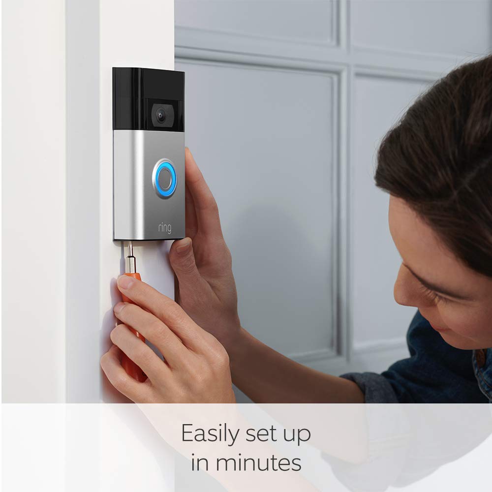 This image shows a person installing a Ring Doorbell 2 on the frame of a door. The doorbell has a camera and a blue ring button.