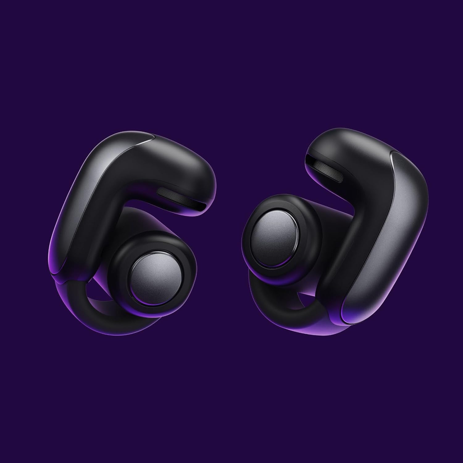The image shows a pair of black Bose Ultra Open earbuds against a purple background. They have a distinctive design with an ergonomic shape that likely fits into the ear and possibly provides noise isolation. The earbuds are clearly modern and look to be of a high-end or premium type, potentially offering features such as touch controls, high-quality audio, and possibly active noise cancellation.