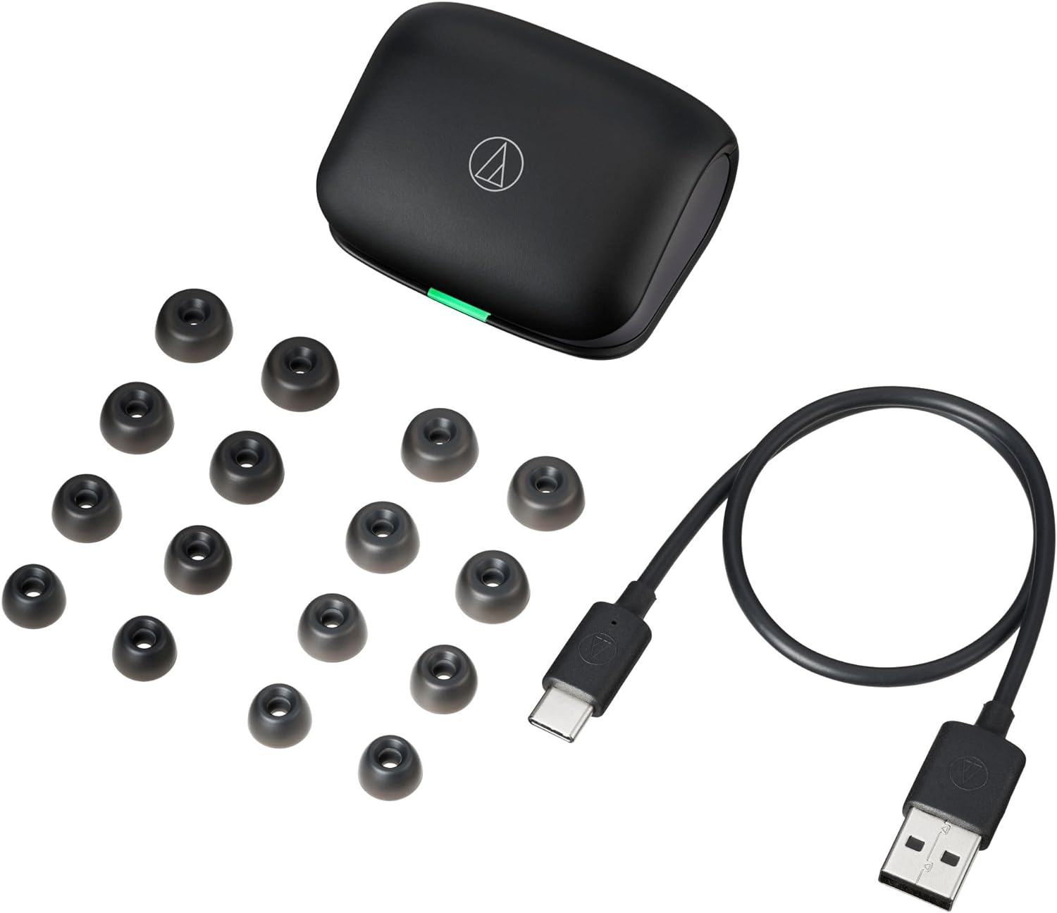 This image displays a set of Audio-Technica ATH-TWX7 earbuds with their charging case, a collection of ear tips in various sizes, and a USB charging cable. The charging case has an LED indicator (visible through the green part) to show the battery status. The USB cable appears to have a USB-A connector on one end and a USB-C connector on the other, suggesting that the case charges via USB-C. The range of ear tips indicates that they are meant to provide users with options for a comfortable and secure fit in the ear canal. The branding on the case and the cable suggests that the product is from Audio-Technica, a company known for making audio equipment.