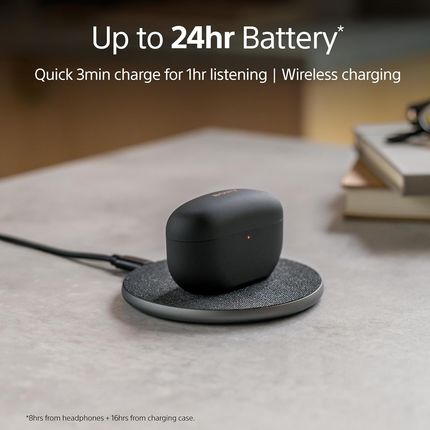 The image shows a charging case for Sony WF-1000XM5 earbuds that is resting on a circular wireless charging pad. A USB cable is plugged into the charging pad, indicating that it's being powered.