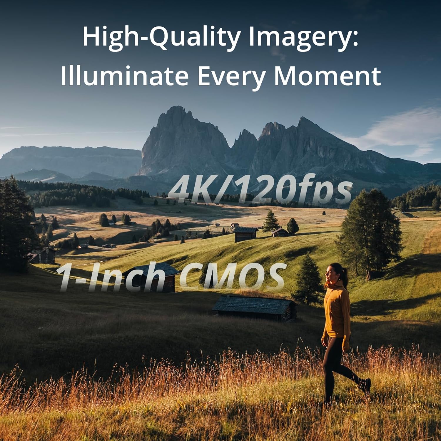The image displays a scenic landscape view with text overlay that appears to be advertising camera capabilities. In the foreground, there is a person walking through a field with tall grass illuminated by sunlight. The individual is wearing a yellow top and black pants. In the background, we can see rolling hills, some trees, and several traditional wooden structures which could possibly be huts or small barns. Dominating the background is a mountain with a distinctive jagged peak, suggesting the scene could be set in a mountainous region. The sky is clear and blue, which contributes to the serene and picturesque environment.