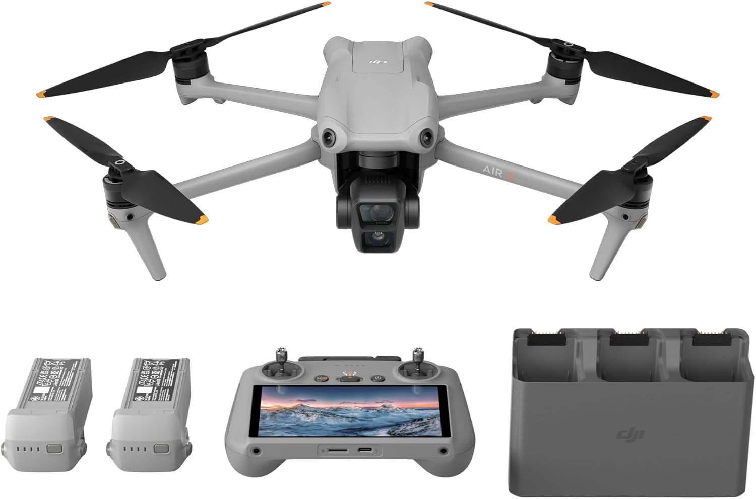 The image shows a DJI Air 3 and its accessories. At the center, there is a quadcopter drone with a camera attached to its underside. The propellers are visible in black with orange tips. Below the drone image, there are two battery packs to the left, indicating that these are spare batteries for extended flight sessions. In the middle, there is a remote control with a built-in display, which is likely used for navigating and controlling the drone. Lastly, on the right side, there is a battery charging hub with slots for multiple batteries, which is used for charging the drone's batteries. The logo on the drone and the charging hub indicates it is manufactured by DJI, which is a well-known drone manufacturer.